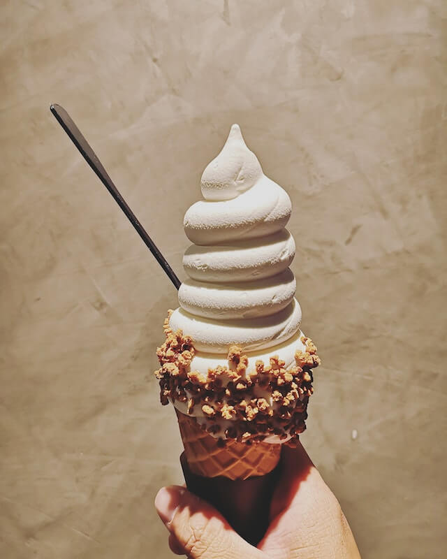 A person holding a vanilla ice cream cone with chocolate and peanut topping