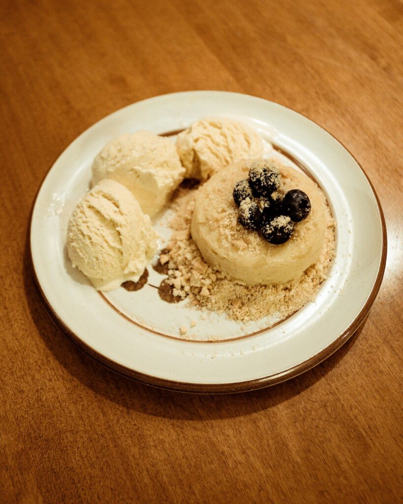 A white plate sitting on the table with an ice cream dessert and berries.
