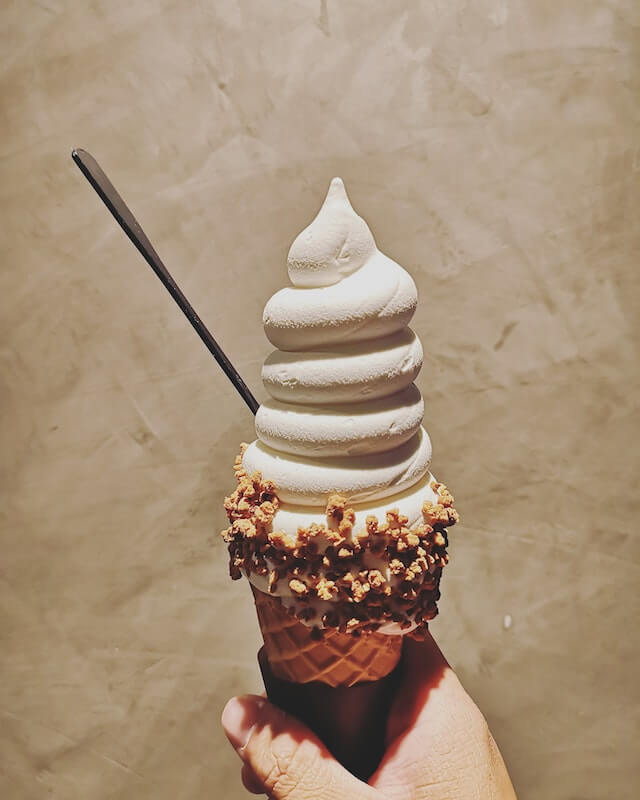 Hand holding a vanilla ice cream cone in a waffle cone.