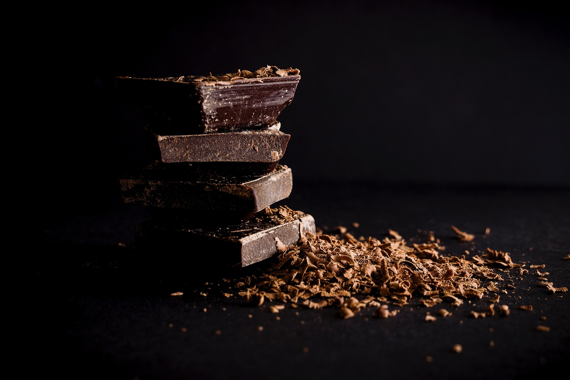 A dark chocolate bar broken and ground into pieces with a black background
