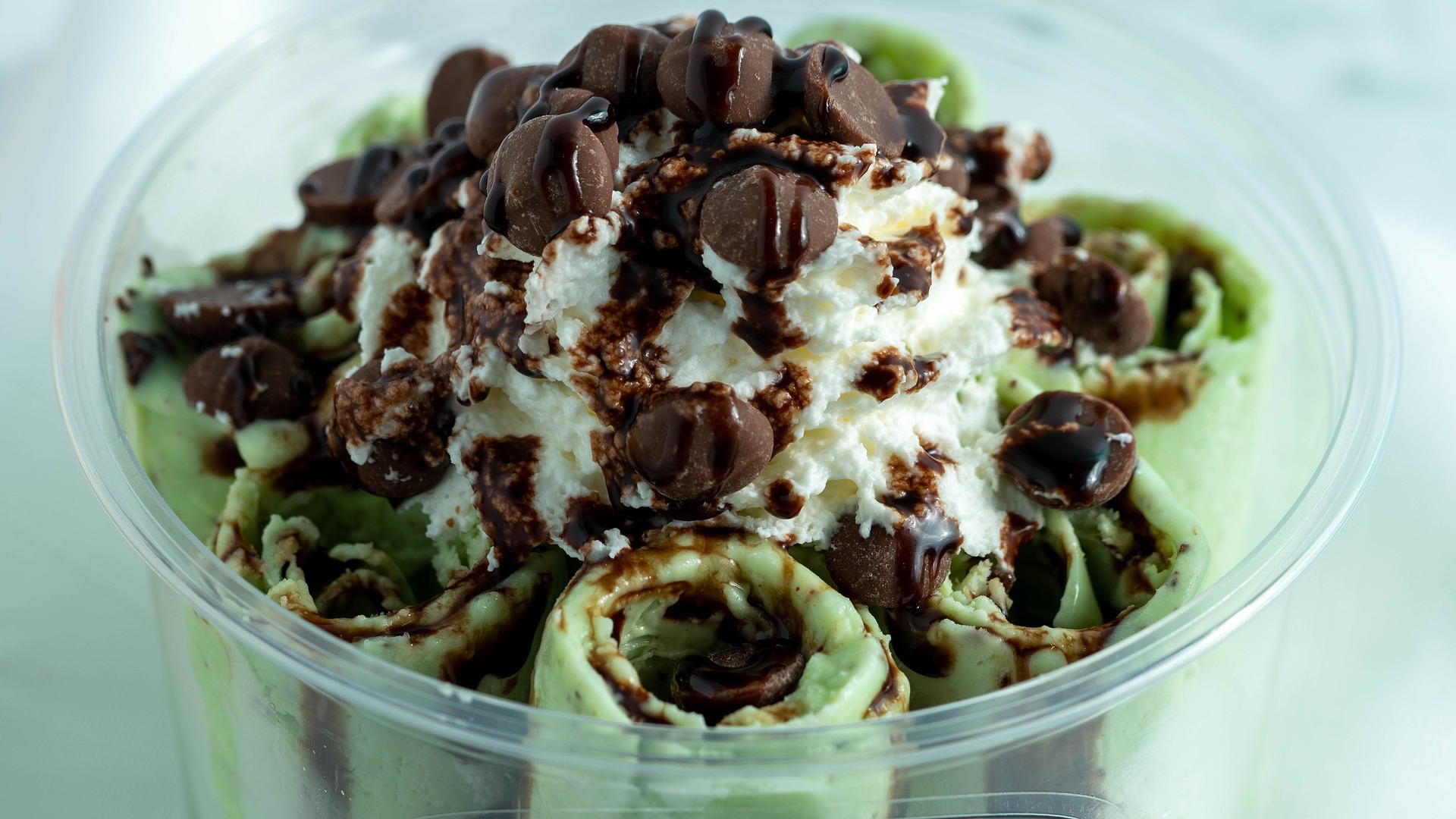 Mint ice cream rolls displayed in a transparent cup with chocolate chips on top