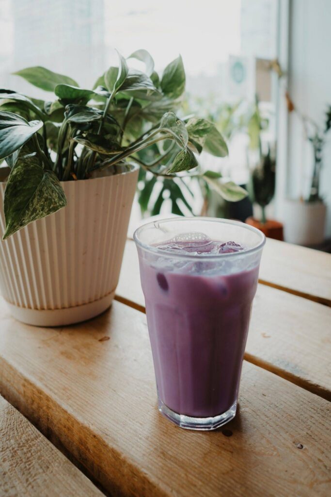 A purple ube beverage served over ice on a wooden table.